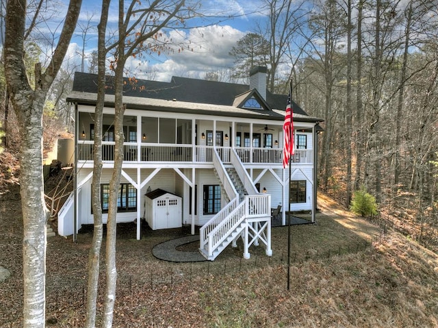 back of property with stairs, a ceiling fan, roof with shingles, and a chimney