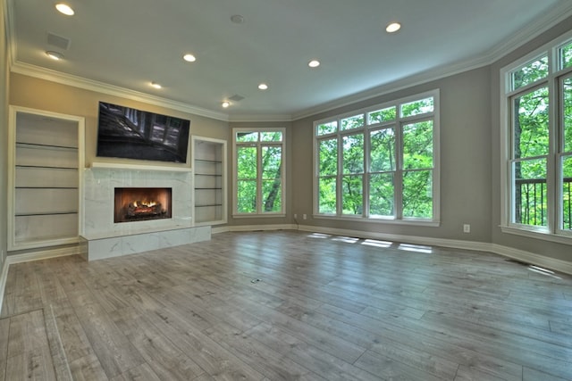 unfurnished living room featuring hardwood / wood-style floors, built in shelves, a premium fireplace, and ornamental molding