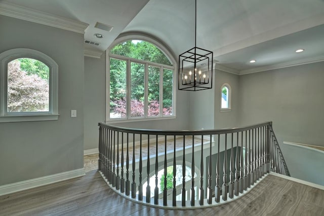 corridor with hardwood / wood-style flooring, ornamental molding, and an inviting chandelier