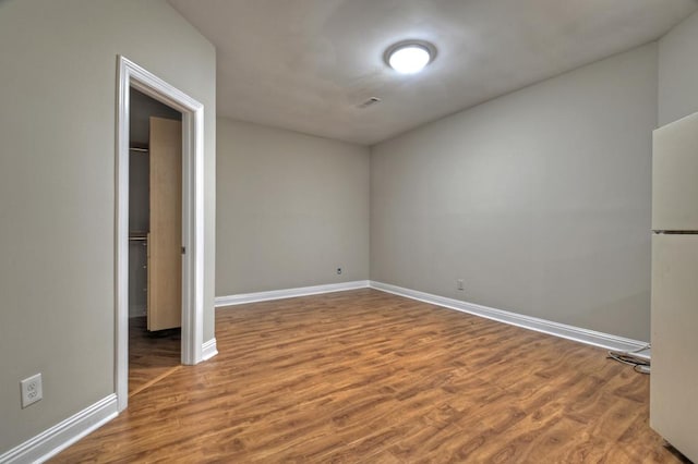 unfurnished bedroom featuring white fridge, wood-type flooring, and a closet