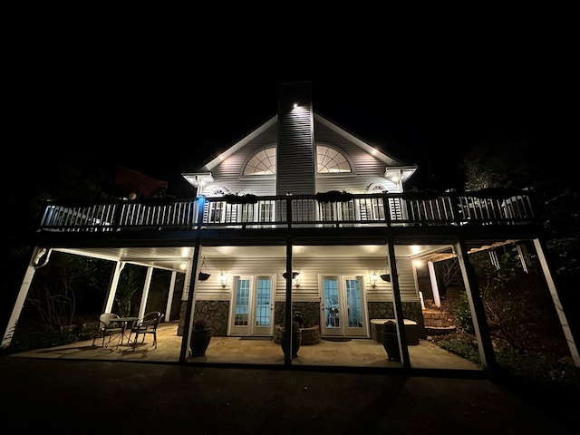 back house at night featuring a patio area, a wooden deck, and french doors