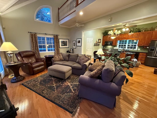 living room with ceiling fan with notable chandelier, hardwood / wood-style flooring, high vaulted ceiling, and ornamental molding