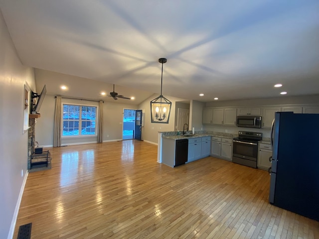 kitchen featuring a stone fireplace, pendant lighting, sink, black appliances, and light wood-type flooring