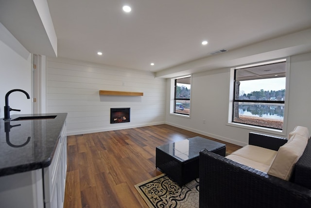 living room featuring dark wood-style flooring, recessed lighting, visible vents, a large fireplace, and wood walls