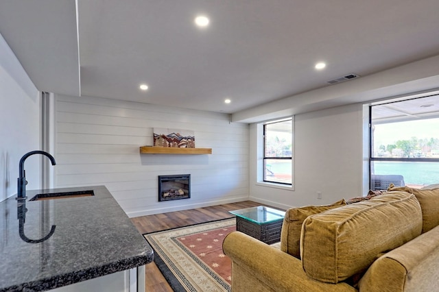 living area with visible vents, a glass covered fireplace, wood finished floors, wood walls, and recessed lighting