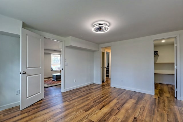 unfurnished bedroom with a spacious closet, a closet, wood finished floors, and baseboards