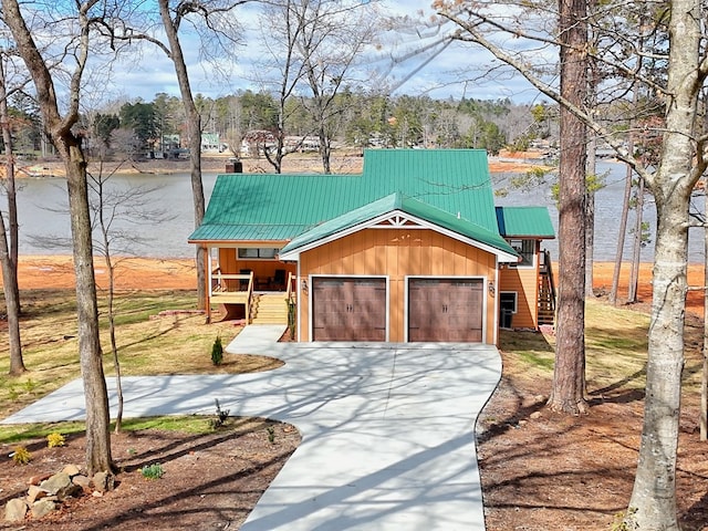 rustic home with covered porch, a water view, concrete driveway, an attached garage, and metal roof