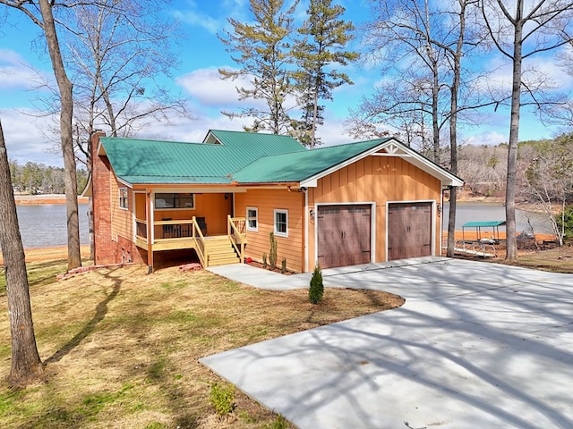 view of front of house featuring a chimney, covered porch, metal roof, driveway, and a front lawn