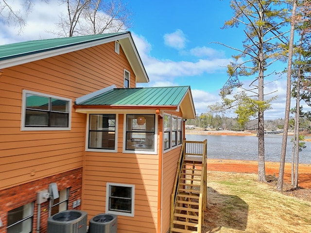 view of property exterior with a water view, stairs, central AC unit, and metal roof