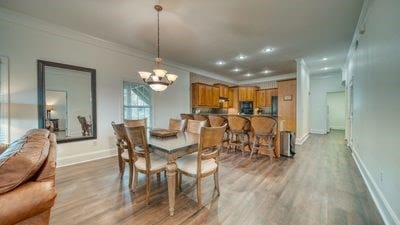 dining area featuring light hardwood / wood-style flooring, ornamental molding, and a notable chandelier