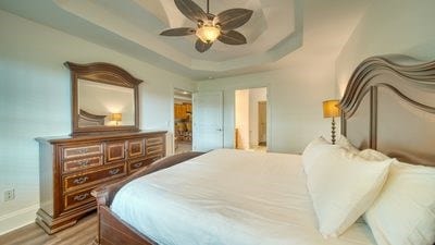 bedroom featuring ceiling fan, a raised ceiling, and wood-type flooring