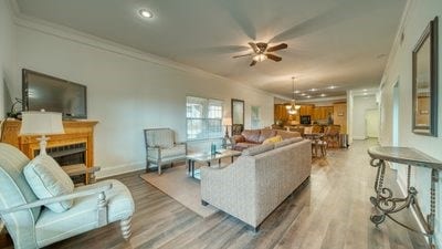 living room with crown molding, ceiling fan, and wood-type flooring