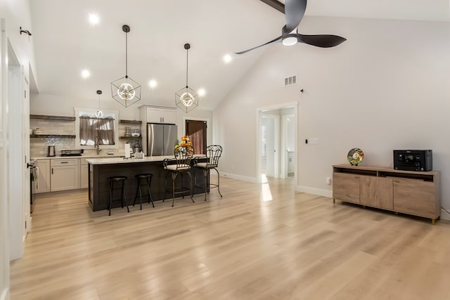 kitchen featuring pendant lighting, a breakfast bar, stainless steel refrigerator, an island with sink, and white cabinets