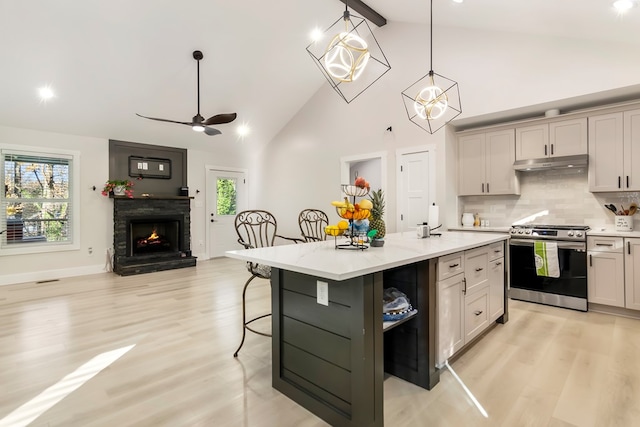 kitchen featuring decorative light fixtures, a kitchen bar, stainless steel range with gas cooktop, an island with sink, and light stone counters