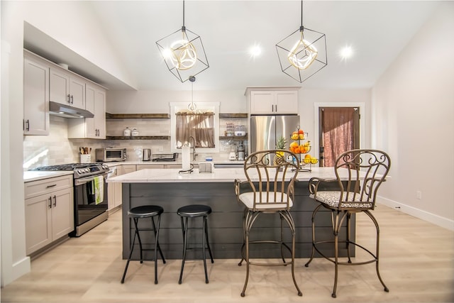 kitchen with hanging light fixtures, appliances with stainless steel finishes, and a center island with sink