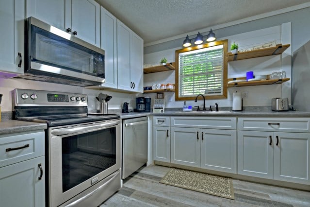 151 Padget Ln, Ellijay, GA 30540 - kitchen with appliances with stainless steel finishes, a sink, open shelves, light wood-style flooring, and a textured ceiling