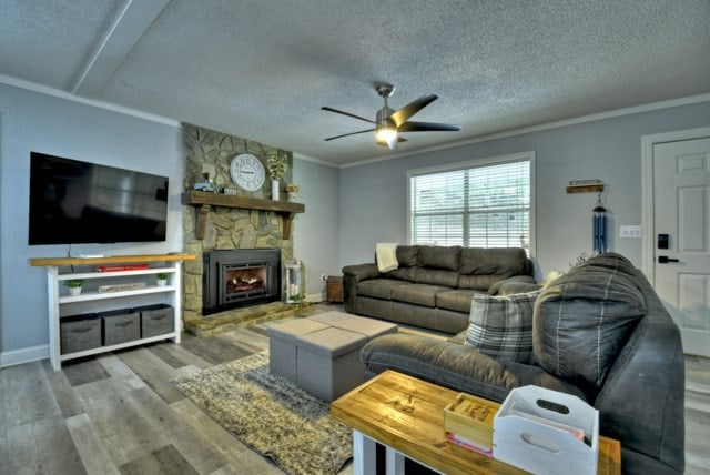 151 Padget Ln, Ellijay, GA 30540 - living room with a ceiling fan, wood finished floors, a textured ceiling, a stone fireplace, and ornamental molding