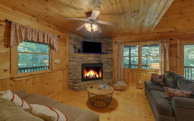 living room with ceiling fan, wood-type flooring, wooden ceiling, a fireplace, and wood walls