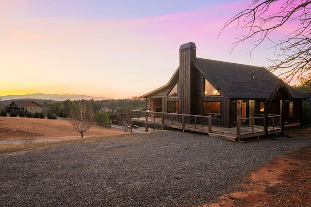 exterior space featuring a wooden deck, roof with shingles, and a chimney