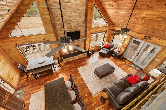 living room featuring wooden walls, wood ceiling, wood finished floors, high vaulted ceiling, and a ceiling fan