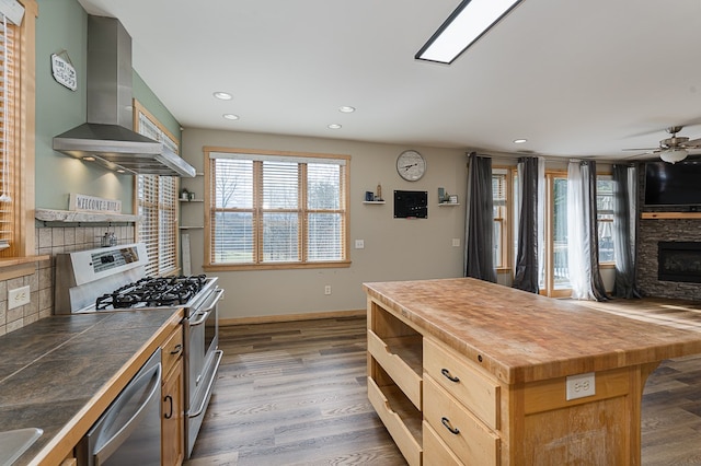 kitchen featuring stainless steel appliances, a kitchen island, wall chimney range hood, dark hardwood / wood-style flooring, and ceiling fan