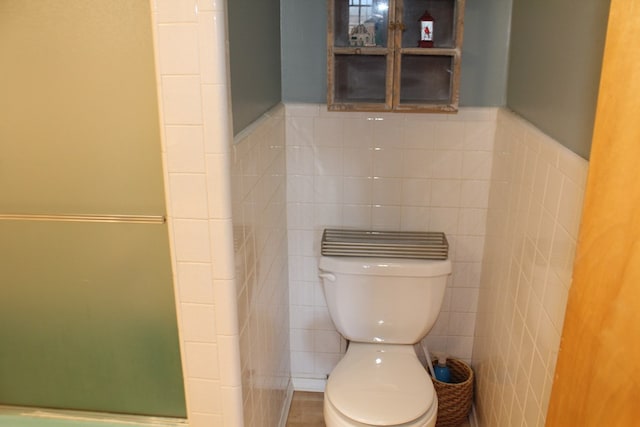 bathroom featuring toilet, tile walls, and a shower with shower door