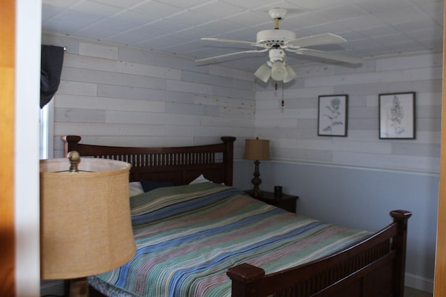 bedroom with ceiling fan and wood walls