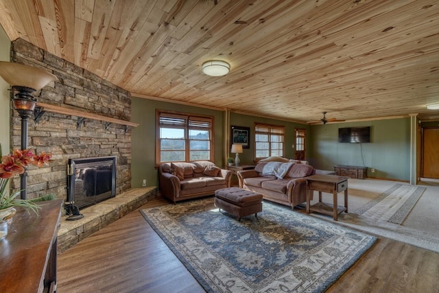 living room featuring a stone fireplace, wood-type flooring, ornamental molding, ceiling fan, and wooden ceiling