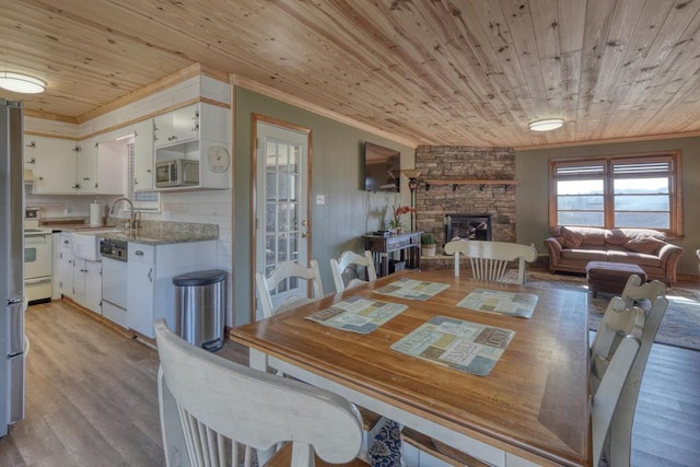 dining area featuring ornamental molding, a stone fireplace, light wood-type flooring, and wooden ceiling