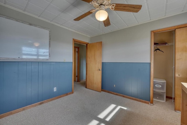 unfurnished bedroom with ceiling fan, light colored carpet, a closet, and wood walls