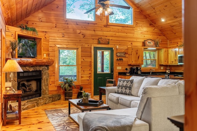 living room featuring sink, ceiling fan, a fireplace, wooden ceiling, and light wood-type flooring