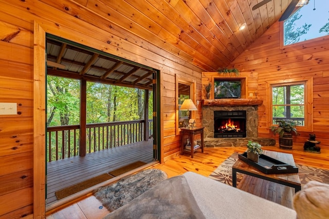 living room featuring wood ceiling, wooden walls, wood-type flooring, a stone fireplace, and vaulted ceiling