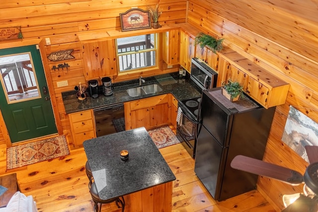 kitchen featuring sink, black appliances, light hardwood / wood-style floors, and wood walls