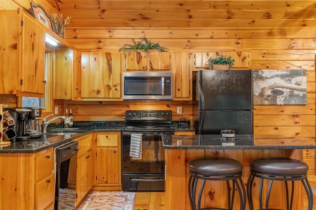 kitchen featuring sink, wood walls, a kitchen breakfast bar, and black appliances