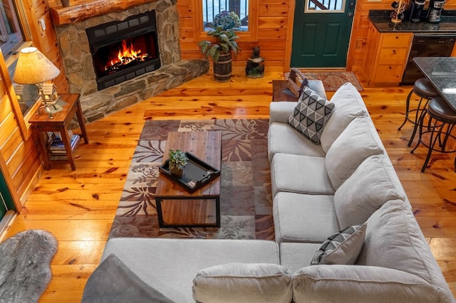 living room featuring a stone fireplace, hardwood / wood-style floors, and wood walls