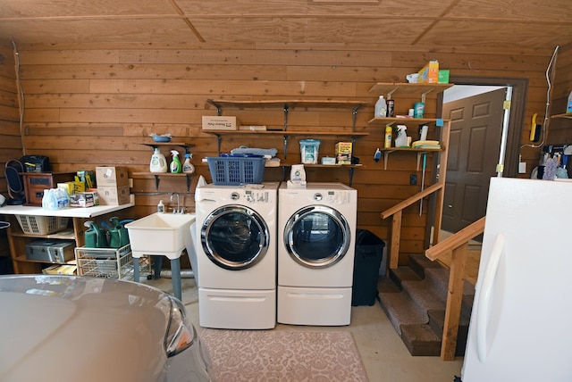 clothes washing area featuring washer and dryer, sink, and wood walls