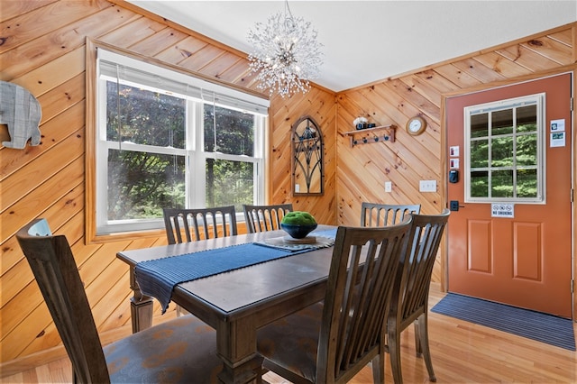 dining room with an inviting chandelier, light wood-type flooring, a wealth of natural light, and wood walls