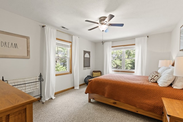 bedroom with ceiling fan, light carpet, multiple windows, and a textured ceiling