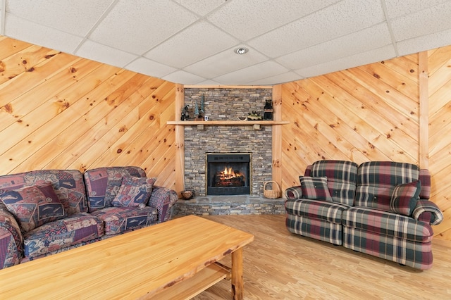 living room with wood-type flooring, a fireplace, a drop ceiling, and wood walls