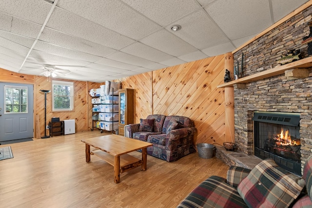 living room with a paneled ceiling, wooden walls, ceiling fan, a fireplace, and hardwood / wood-style floors