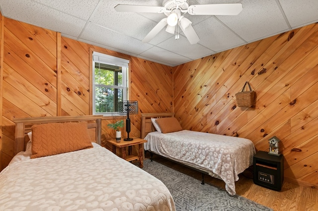 bedroom featuring wood-type flooring, a paneled ceiling, ceiling fan, and wood walls