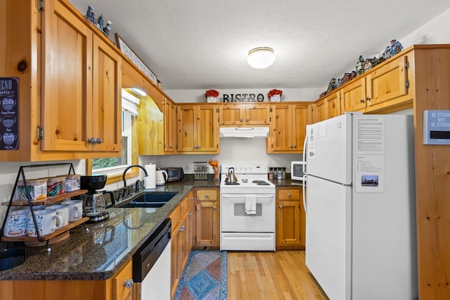 kitchen with sink, white appliances, light hardwood / wood-style flooring, dark stone countertops, and a textured ceiling