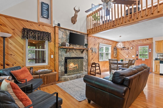 living room with ceiling fan, wooden walls, a towering ceiling, a fireplace, and light hardwood / wood-style floors