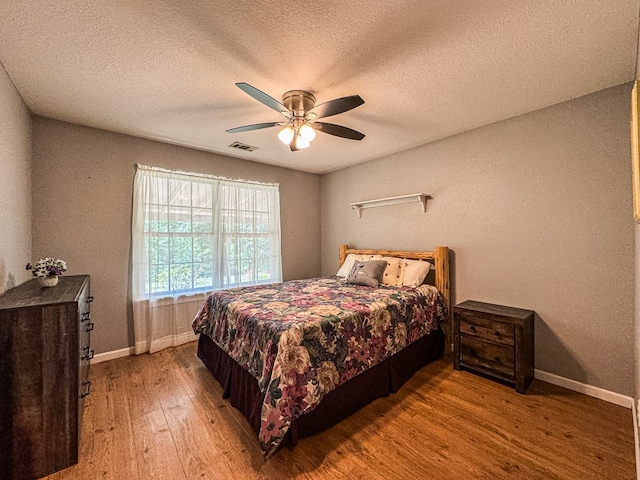 bedroom with a textured ceiling, wood-type flooring, and ceiling fan