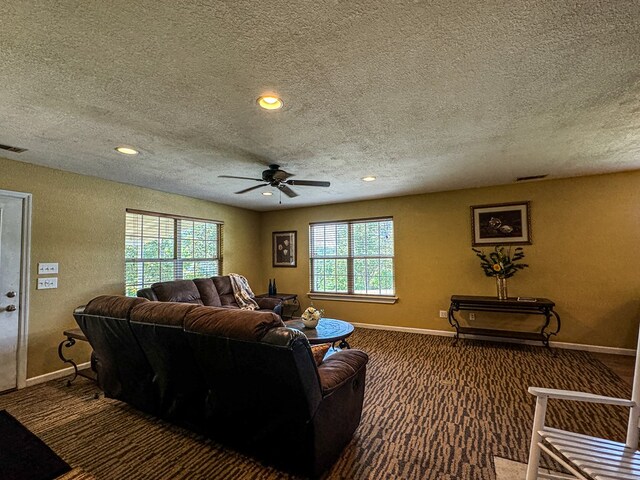 living room featuring dark carpet, ceiling fan, plenty of natural light, and a textured ceiling