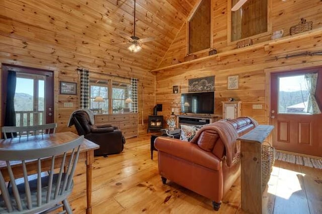 living area featuring high vaulted ceiling, wood walls, wood ceiling, light wood finished floors, and a wood stove