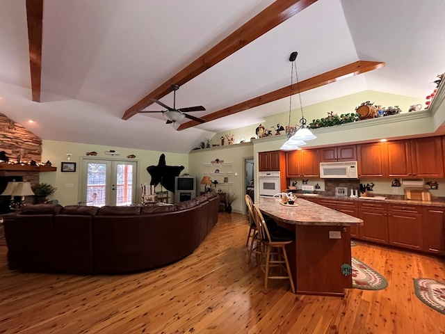 kitchen with a kitchen bar, vaulted ceiling with beams, light hardwood / wood-style floors, and white appliances