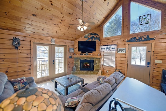 tiled living room featuring wood ceiling, a stone fireplace, high vaulted ceiling, wood walls, and ceiling fan