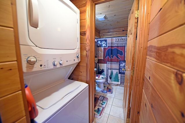 laundry area featuring light tile patterned floors, stacked washer and clothes dryer, wood walls, and wood ceiling