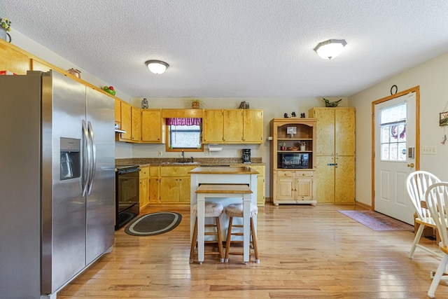 kitchen featuring under cabinet range hood, stainless steel fridge, stove, and light wood finished floors